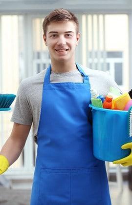 Employee looking at camera holding a bucket of cleaning supplies